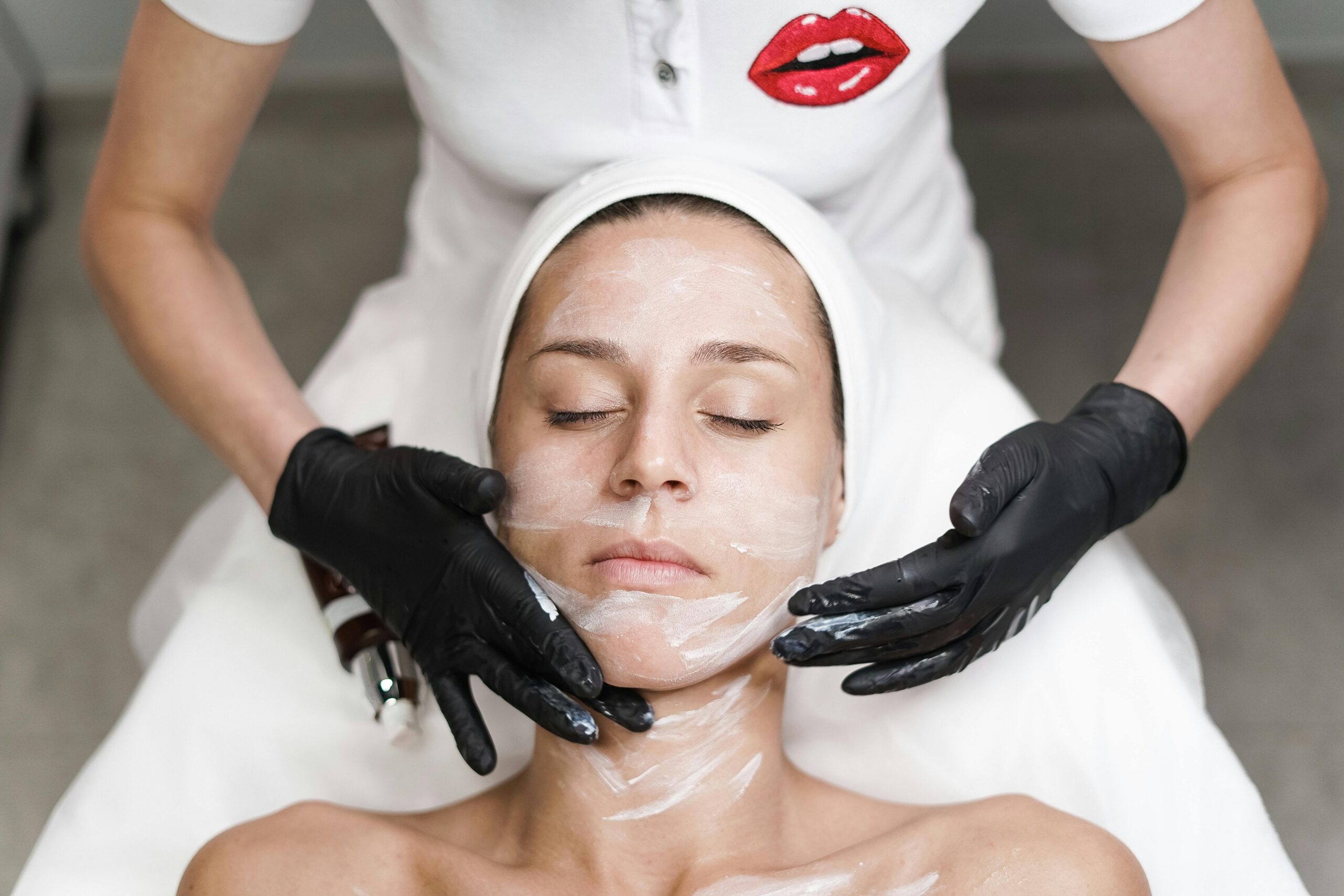 Woman receiving a facial treatment at spa, with beautician applying mask in a relaxing setting.