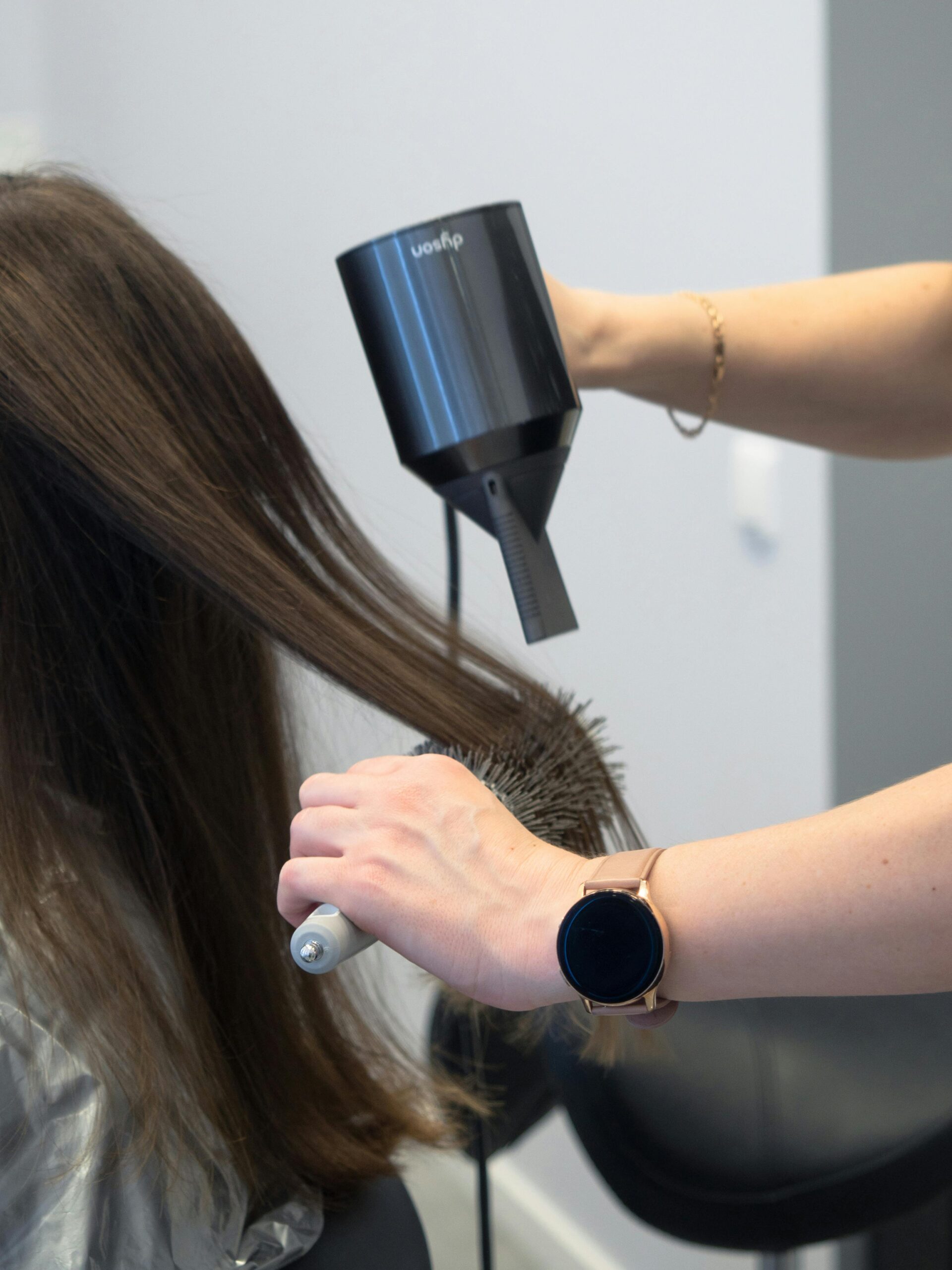 Close-up of a hairdresser using a hairdryer and brush for styling in a salon.