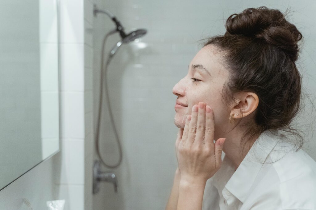 How to Remove Tan From Your Face Fast: 10 Effective Home & Skincare Tips A woman applying facial cream in a mirror for her skincare routine in a bathroom.