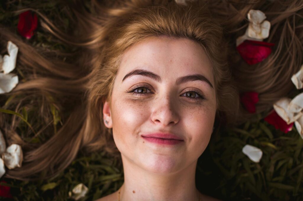 How to Make Your Skin Glow Naturally: 12 Proven Tips for Radiant Skin Portrait of a smiling young woman with rose petals in her hair, lying on grass outdoors.