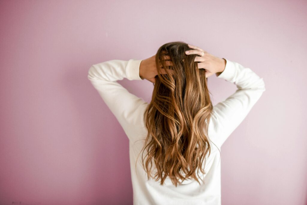 How Can I Permanently Stop Hair Loss? A Complete Guide Back view of a woman with elegant long brown hair against a pink wall, showcasing stylish hair design.